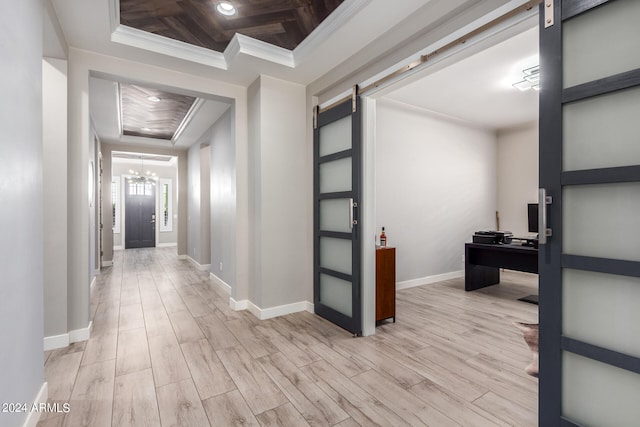 hall featuring a barn door, a tray ceiling, crown molding, and light hardwood / wood-style flooring