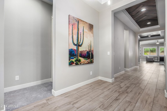 corridor with a tray ceiling and light hardwood / wood-style flooring