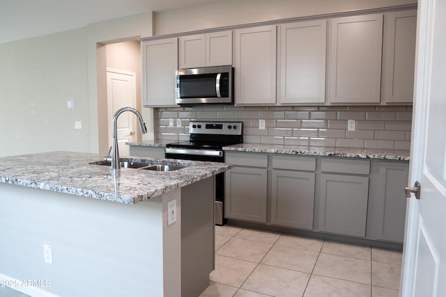 kitchen with sink, light stone counters, gray cabinets, stainless steel appliances, and decorative backsplash