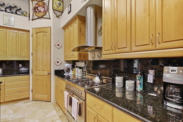 kitchen with wall chimney range hood, light tile patterned floors, dark stone countertops, decorative backsplash, and gas range