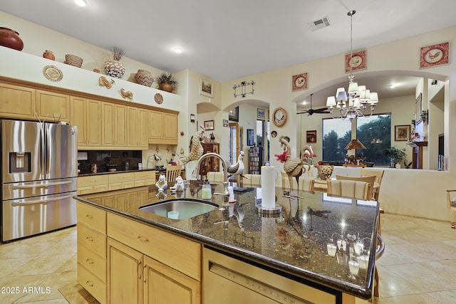 kitchen with sink, stainless steel fridge with ice dispenser, hanging light fixtures, dark stone countertops, and a kitchen island with sink