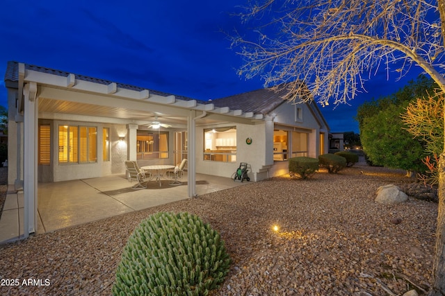 back house at night with ceiling fan and a patio