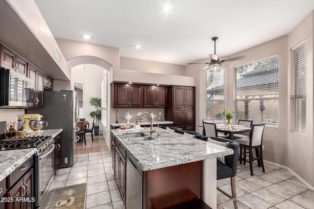 kitchen featuring a center island with sink, arched walkways, ceiling fan, appliances with stainless steel finishes, and a sink