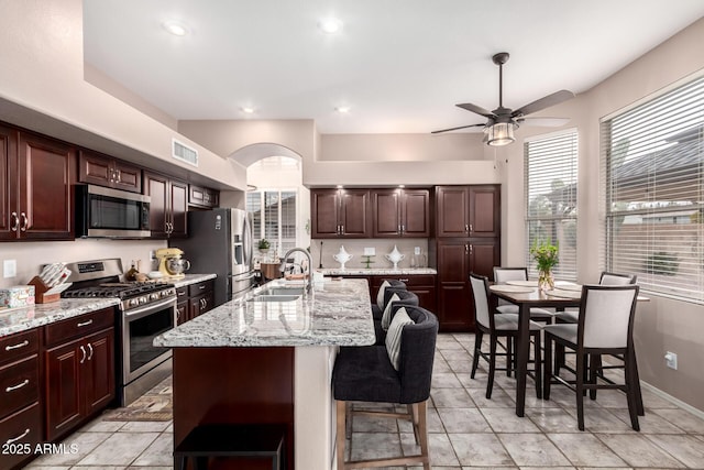 kitchen featuring sink, appliances with stainless steel finishes, a kitchen island with sink, dark brown cabinets, and a kitchen breakfast bar