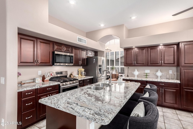 kitchen featuring appliances with stainless steel finishes, an island with sink, sink, a breakfast bar area, and light stone counters