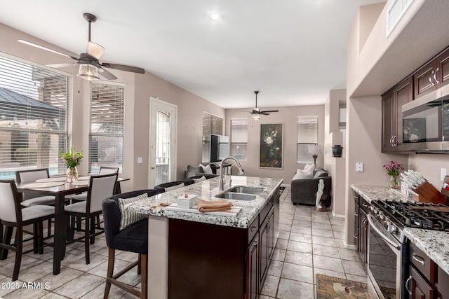 kitchen with stainless steel appliances, a sink, open floor plan, dark brown cabinets, and a kitchen bar