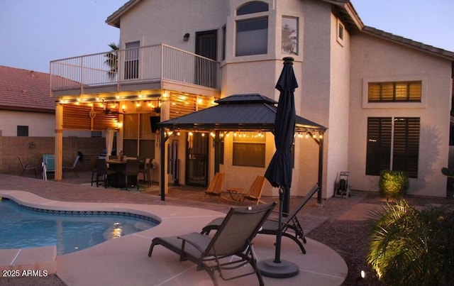 rear view of house with an outdoor pool, a gazebo, a patio area, and stucco siding