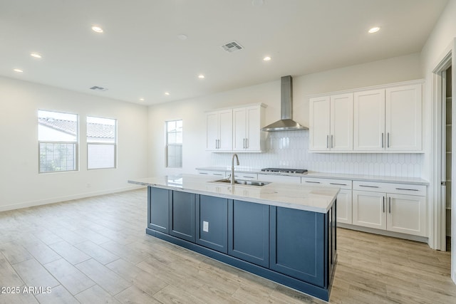 kitchen with visible vents, white cabinets, gas stovetop, wall chimney exhaust hood, and a sink