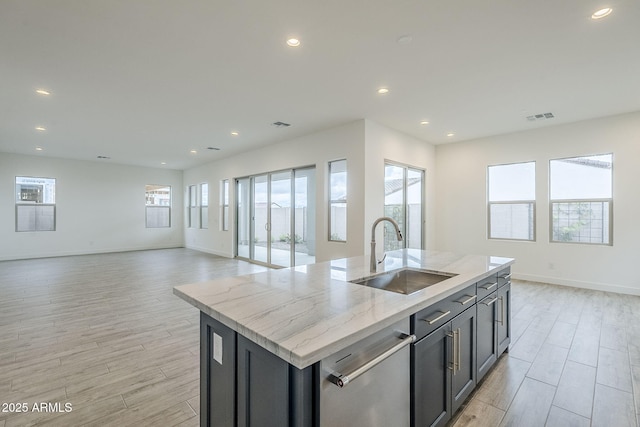 kitchen with light wood-style flooring, an island with sink, a sink, stainless steel dishwasher, and open floor plan