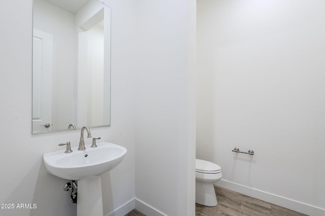 half bath with toilet, wood finished floors, baseboards, and a sink