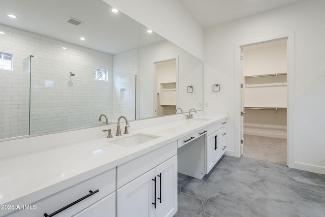 full bath featuring double vanity, visible vents, tiled shower, and a sink