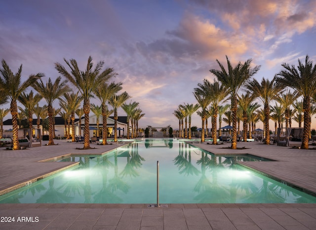 pool at dusk featuring a patio area and a community pool