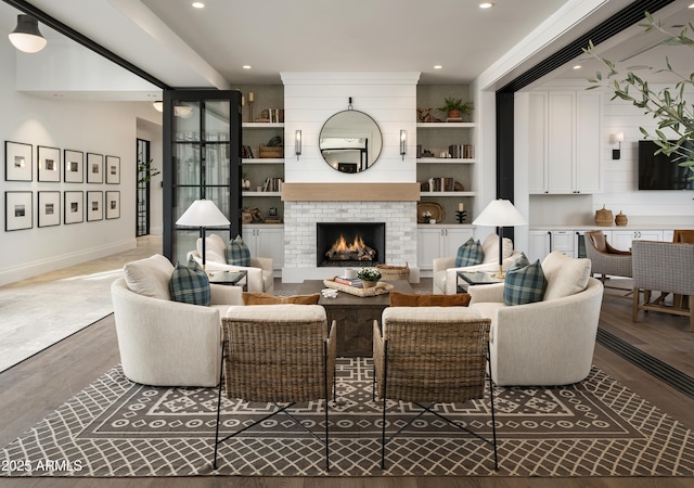 living room featuring baseboards, built in shelves, wood finished floors, and a fireplace