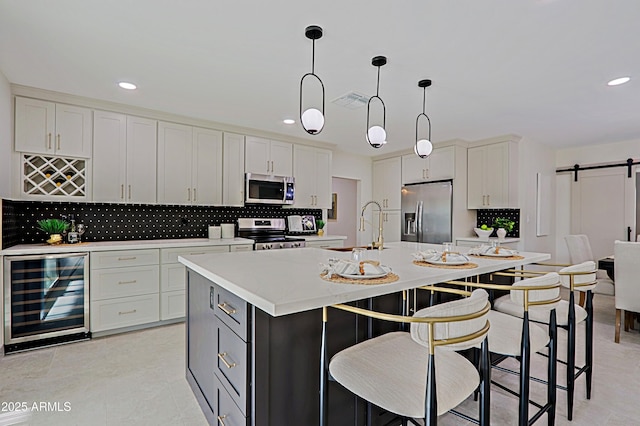 kitchen with a barn door, appliances with stainless steel finishes, a kitchen island with sink, a sink, and beverage cooler