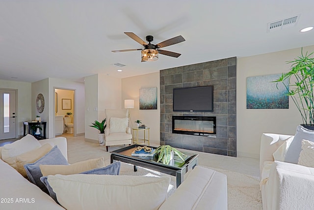 living area featuring baseboards, visible vents, ceiling fan, and a tiled fireplace