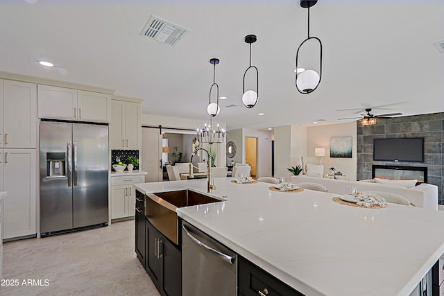 kitchen with a barn door, appliances with stainless steel finishes, open floor plan, a sink, and a multi sided fireplace