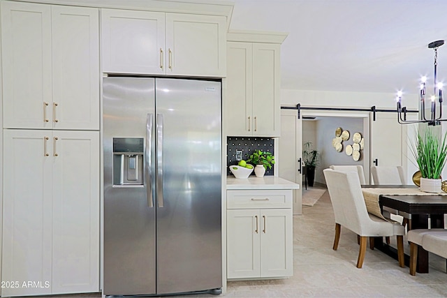 kitchen featuring a barn door, light countertops, decorative backsplash, stainless steel fridge, and decorative light fixtures