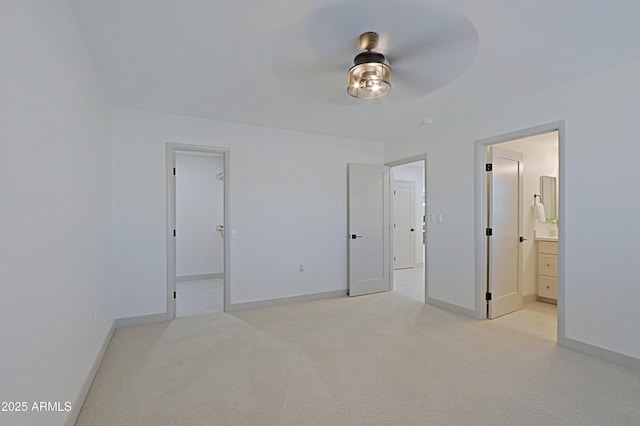 unfurnished bedroom featuring ensuite bathroom, light colored carpet, a ceiling fan, baseboards, and a spacious closet