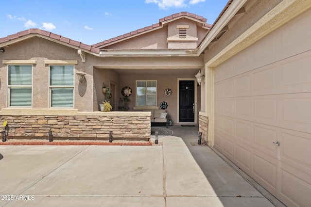 view of exterior entry with a garage, stone siding, a tile roof, and stucco siding