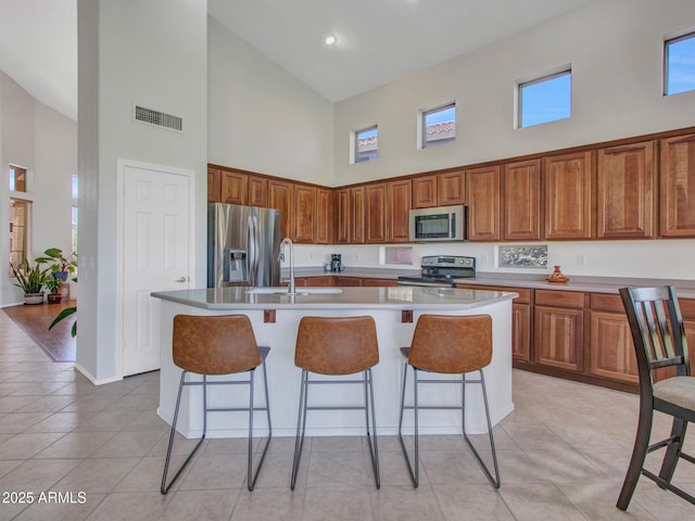 40814 N Majesty Ct, Anthem, AZ 85086 - kitchen featuring a high ceiling, appliances with stainless steel finishes, brown cabinetry, a breakfast bar, and a kitchen island with sink