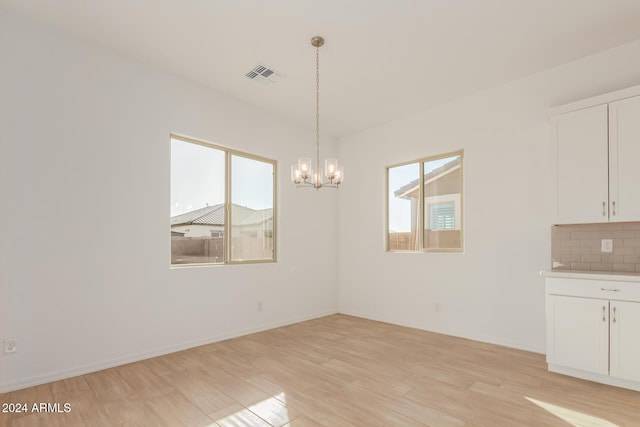 unfurnished dining area featuring a healthy amount of sunlight, light hardwood / wood-style floors, and a chandelier