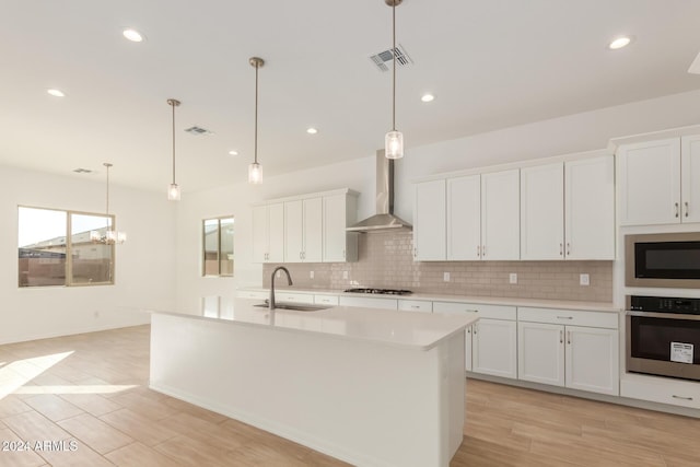 kitchen featuring white cabinets, stainless steel appliances, light hardwood / wood-style floors, and wall chimney range hood