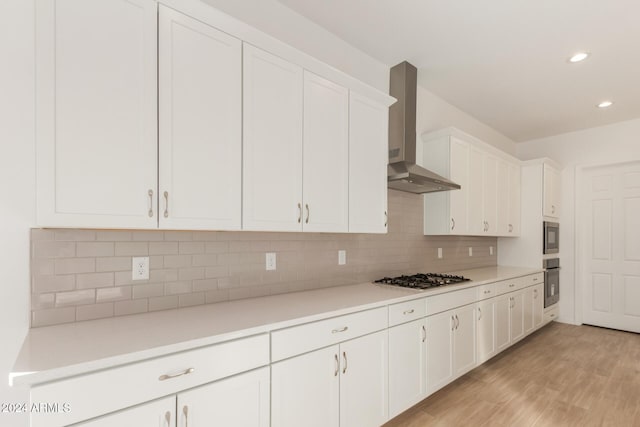 kitchen with white cabinetry, wall chimney exhaust hood, tasteful backsplash, light hardwood / wood-style floors, and appliances with stainless steel finishes