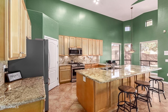 kitchen featuring a center island with sink, a breakfast bar area, appliances with stainless steel finishes, a high ceiling, and a sink