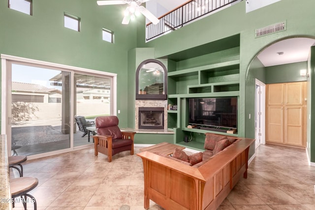 tiled living area featuring built in shelves, arched walkways, visible vents, a fireplace with raised hearth, and ceiling fan