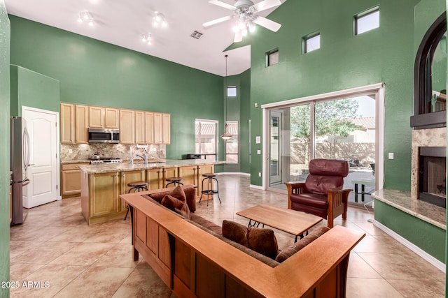 living area with a fireplace, light tile patterned floors, visible vents, a towering ceiling, and ceiling fan