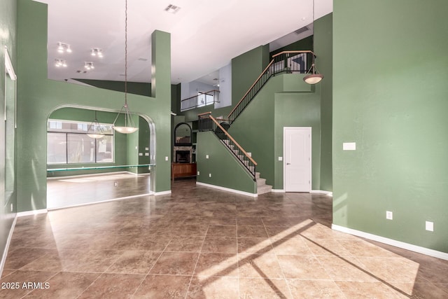 unfurnished living room with arched walkways, a towering ceiling, visible vents, stairs, and baseboards