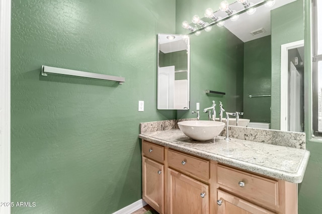 bathroom featuring a textured wall, vanity, visible vents, and baseboards