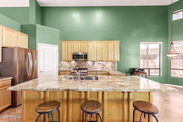 kitchen with stainless steel appliances, a towering ceiling, decorative backsplash, a sink, and a kitchen breakfast bar