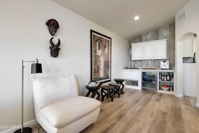 sitting room with bar, light hardwood / wood-style flooring, beverage cooler, and vaulted ceiling