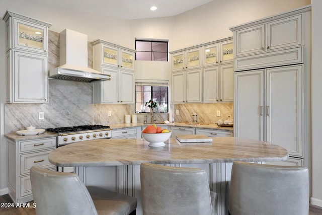 kitchen featuring a center island, a kitchen breakfast bar, wall chimney range hood, light stone countertops, and stainless steel gas cooktop