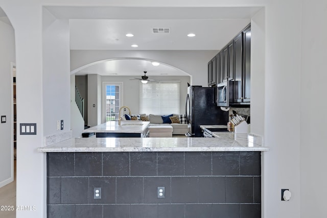 3687 E Leslie Dr, Gilbert, AZ 85296 - kitchen with arched walkways, a ceiling fan, light stone counters, freestanding refrigerator, and stainless steel microwave