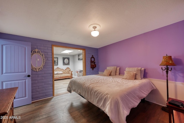 bedroom with a textured ceiling, wainscoting, and wood finished floors