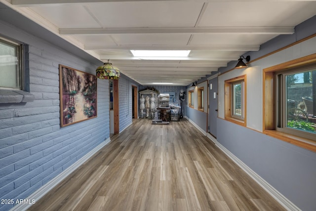 hall with baseboards, beamed ceiling, brick wall, and wood finished floors