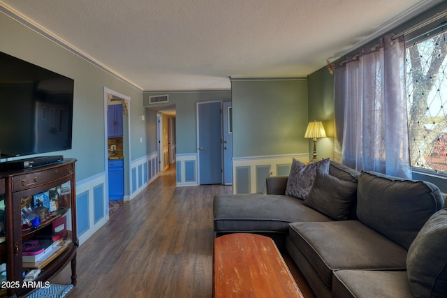 living room featuring visible vents, wainscoting, dark wood-type flooring, a textured ceiling, and a decorative wall