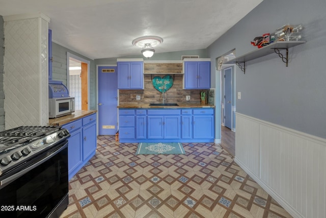 kitchen featuring open shelves, butcher block counters, white microwave, gas range, and blue cabinets