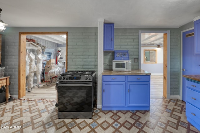 kitchen featuring stainless steel gas stove, white microwave, blue cabinets, and light floors