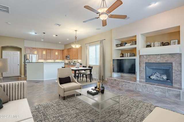 tiled living room with a fireplace, built in shelves, and ceiling fan