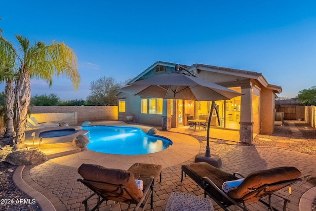 pool at dusk with a patio area and an in ground hot tub