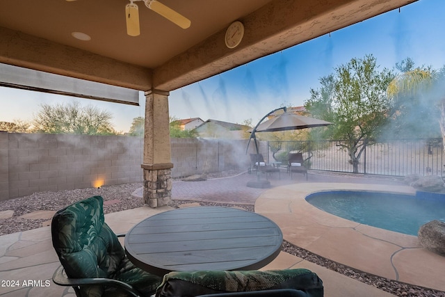 pool at dusk featuring ceiling fan and a patio area