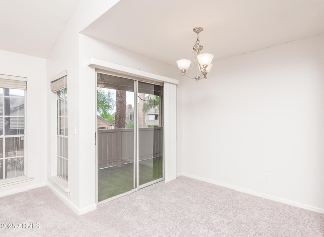 carpeted empty room featuring a chandelier and baseboards