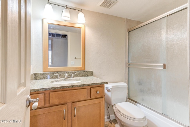 bathroom featuring shower / bath combination with glass door, toilet, visible vents, a textured wall, and vanity