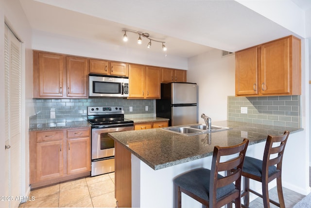 kitchen with a sink, a breakfast bar area, backsplash, a peninsula, and appliances with stainless steel finishes