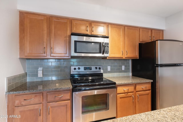 kitchen with light stone countertops, stainless steel appliances, brown cabinetry, and tasteful backsplash