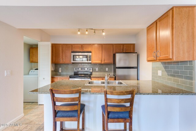 kitchen with a peninsula, a sink, stone countertops, appliances with stainless steel finishes, and washer / dryer