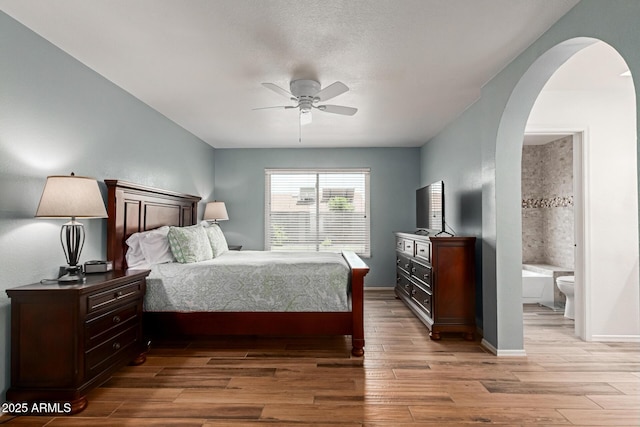 19 W Wickieup Ln, Phoenix, AZ 85027 - bedroom with arched walkways, light wood-type flooring, connected bathroom, a ceiling fan, and baseboards